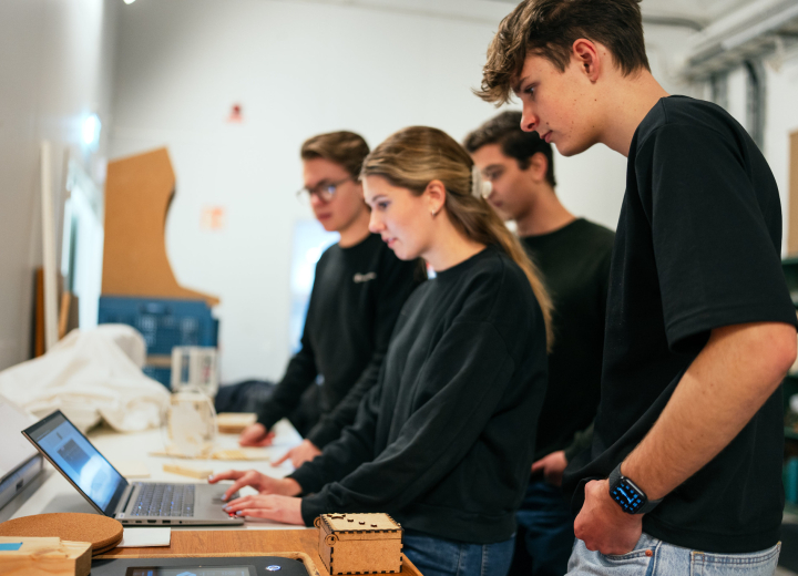 Fyra UF-företagare står i en verkstad och arbetar på en laptop.